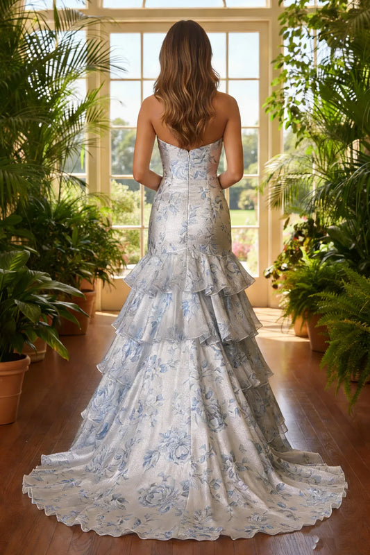 Woman in strapless blue floral ruffled prom gown standing in sunlit indoor garden