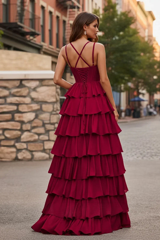 Back view of Sevoba wine red evening gown showing a lace-up corset back, criss-cross straps, and voluminous layered ruffle skirt, street background