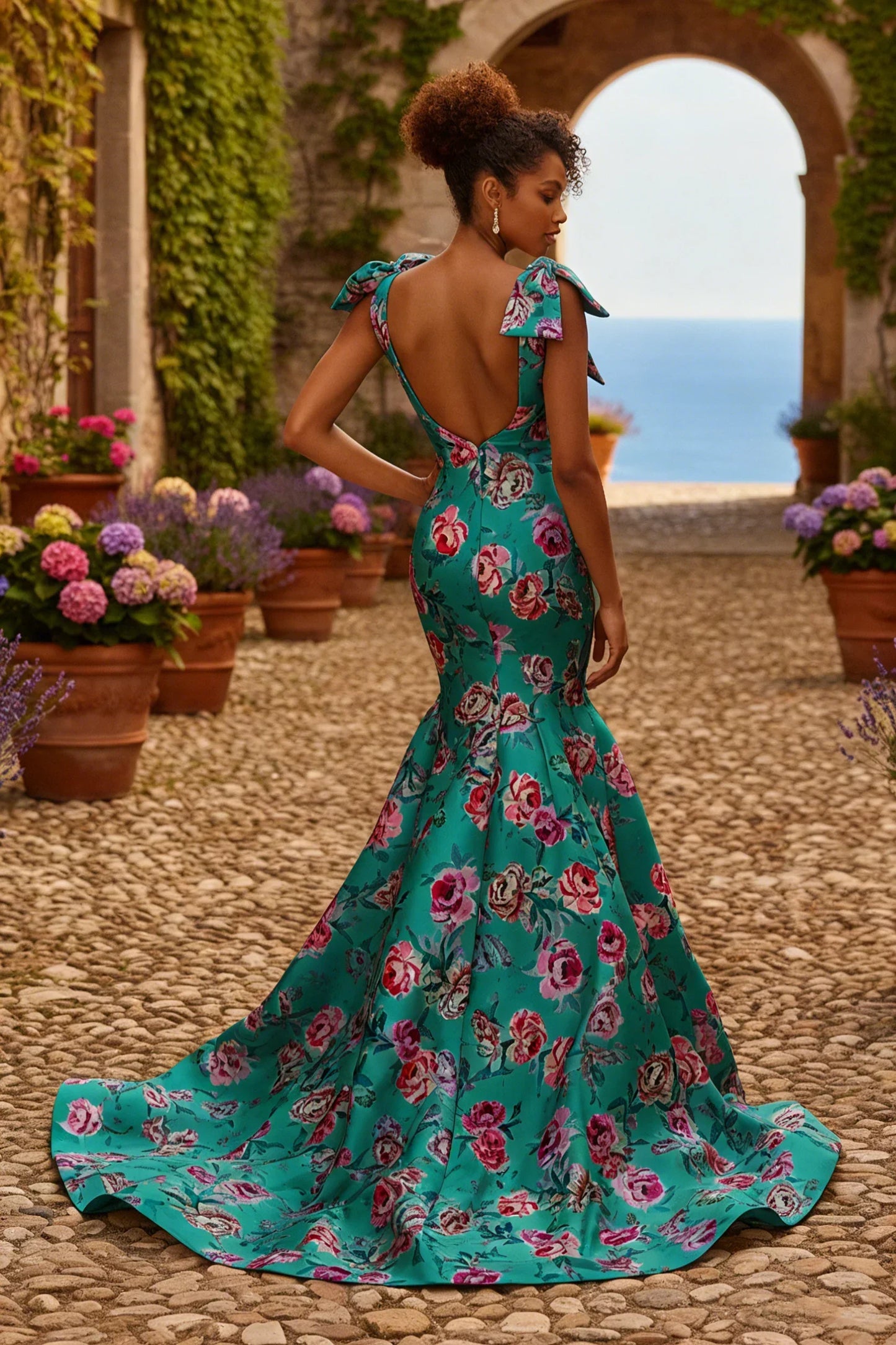 Woman in elegant turquoise floral mermaid gown with open back, outdoors on cobblestone path