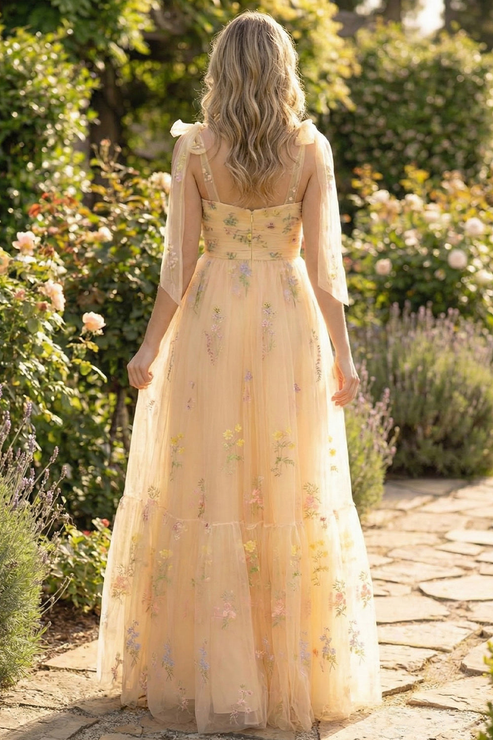 Back view of Sevoba floral embroidered yellow evening gown showing a zipper closure and ruffle tiered skirt, garden path background
