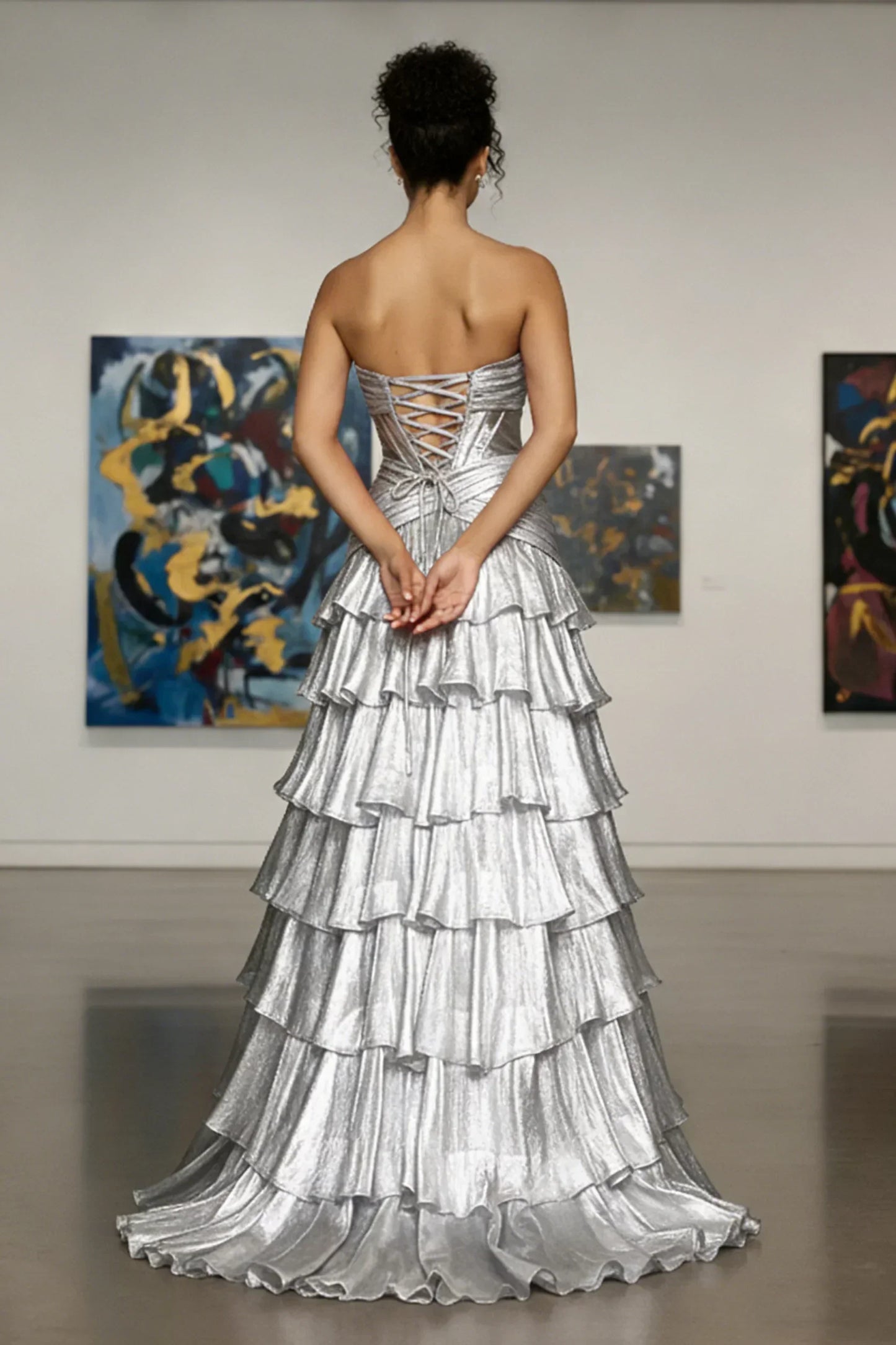 Woman in strapless silver tiered evening gown with lace-up back, standing in art gallery