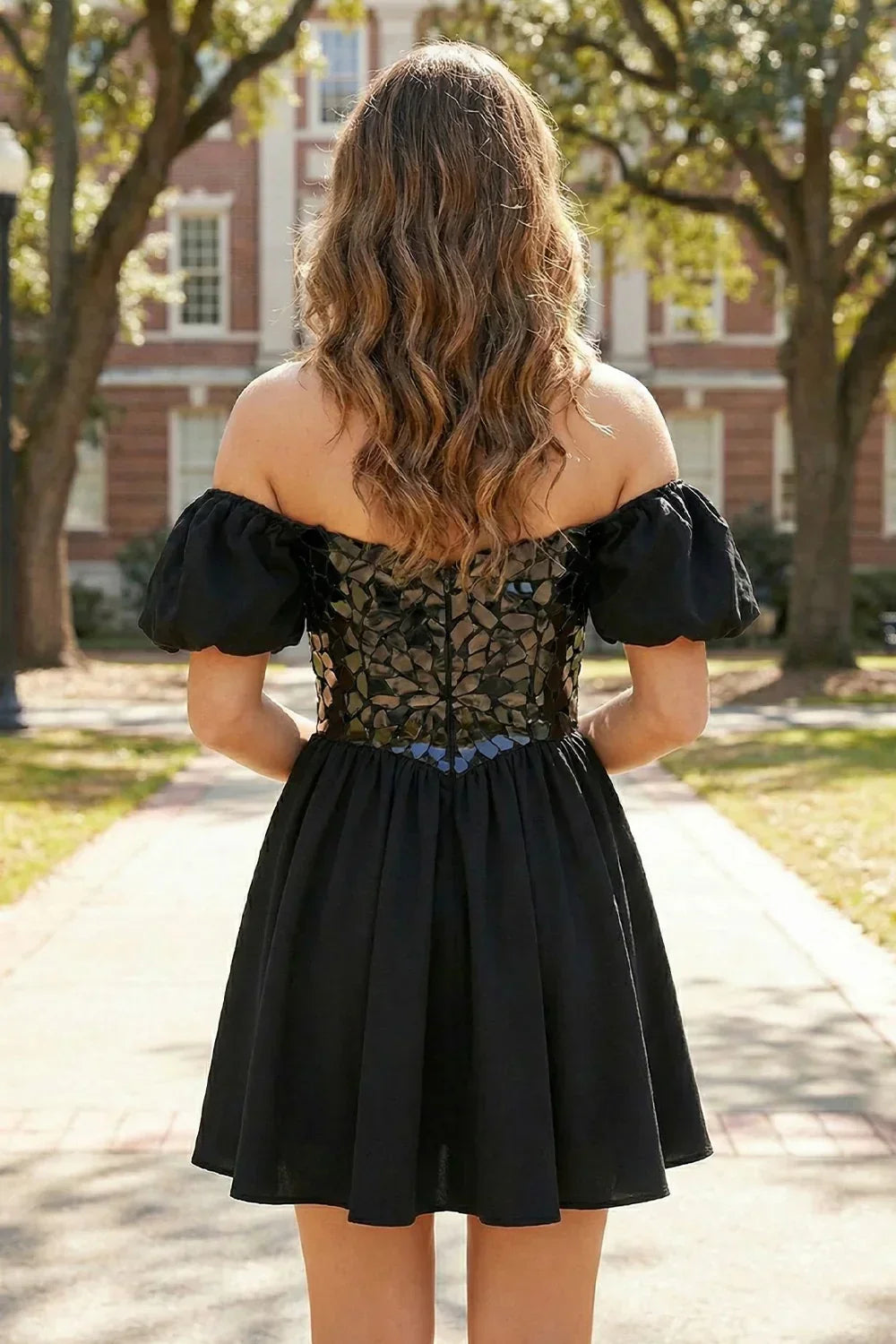 Back view of a woman wearing a short A-line black off shoulder dress with puff sleeves outdoors.