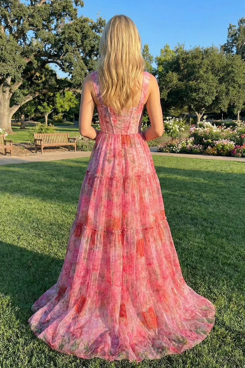 Woman in a long pink floral A-line prom dress standing in a garden