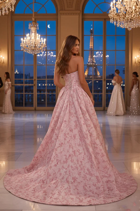 Woman in pink strapless A-line prom dress with floral jacquard fabric and pearl trim in elegant ballroom.