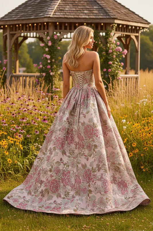 Strapless A-line prom dress with pink floral patterns, worn outdoors by a gazebo.
