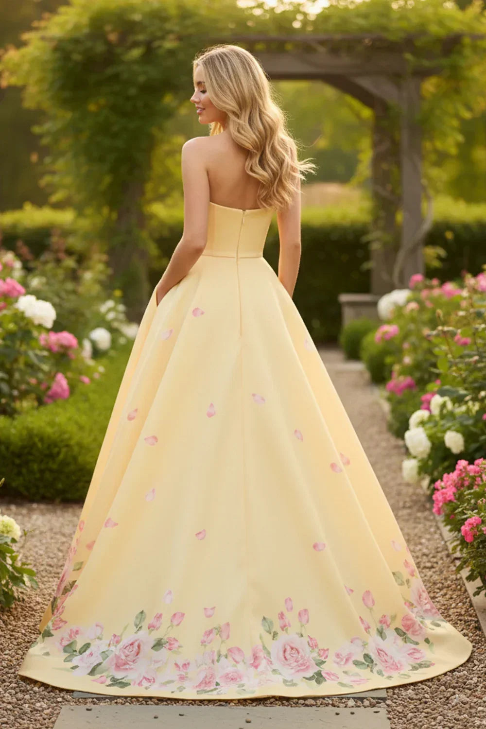 A-line strapless yellow satin prom dress with floral print hem, worn outdoors in a garden.
