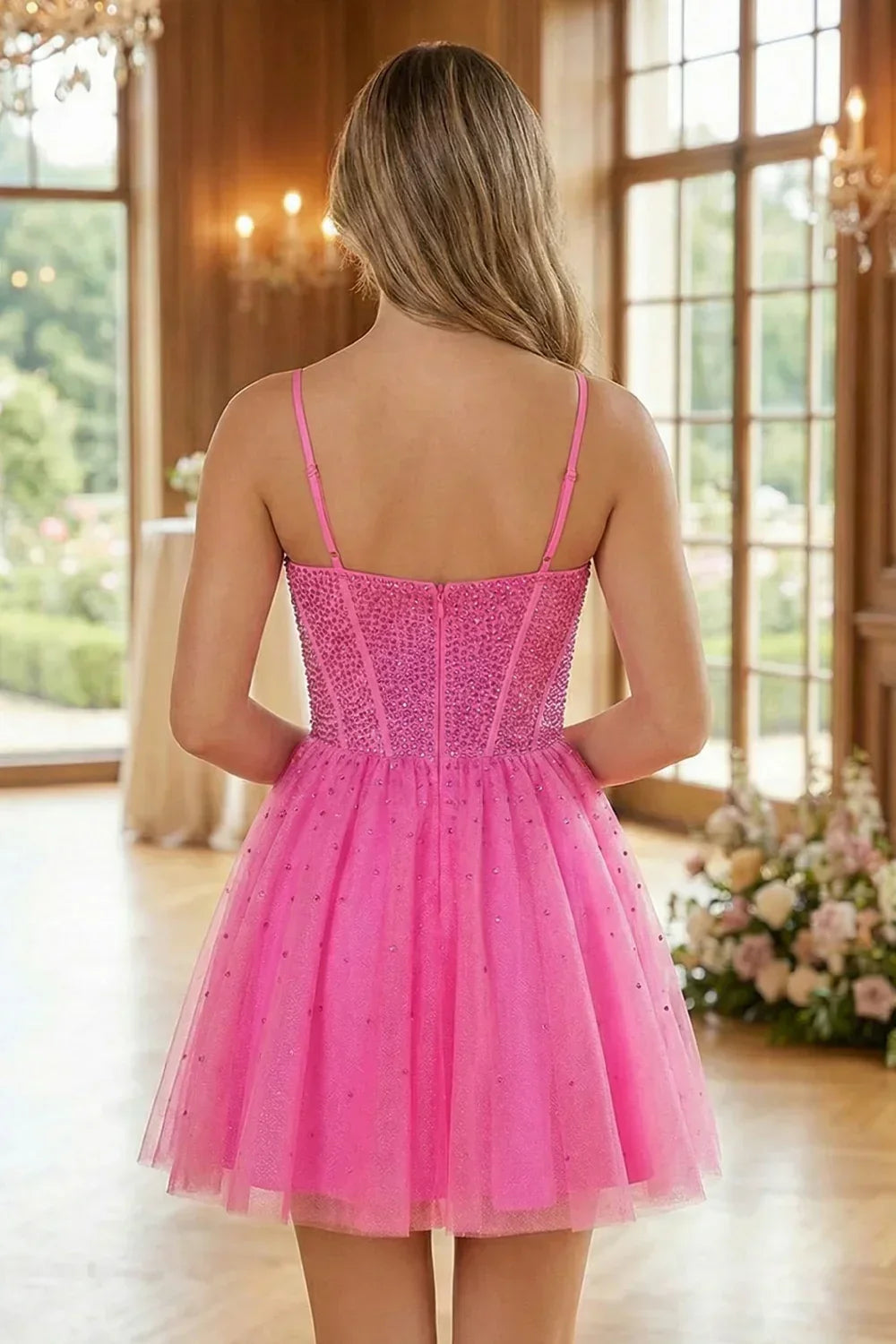 Back view of a pink A-line short homecoming dress with beading, worn indoors near windows.