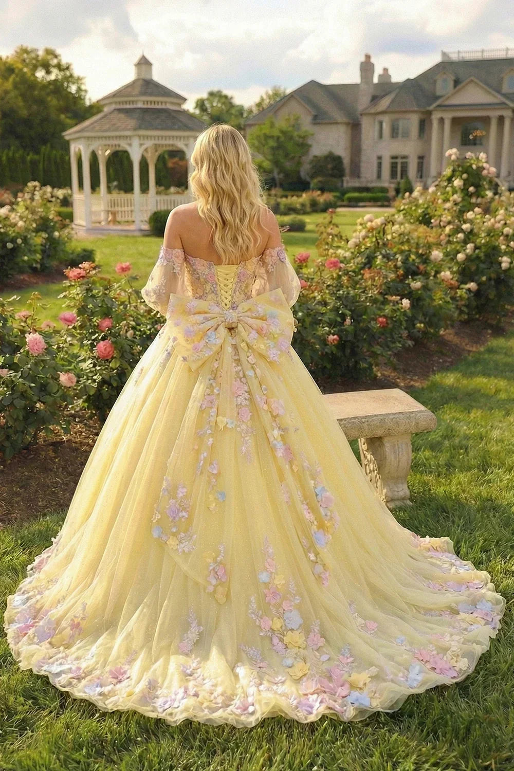 Yellow ball gown with floral lace, off-shoulder and long sheer sleeves, in a garden setting