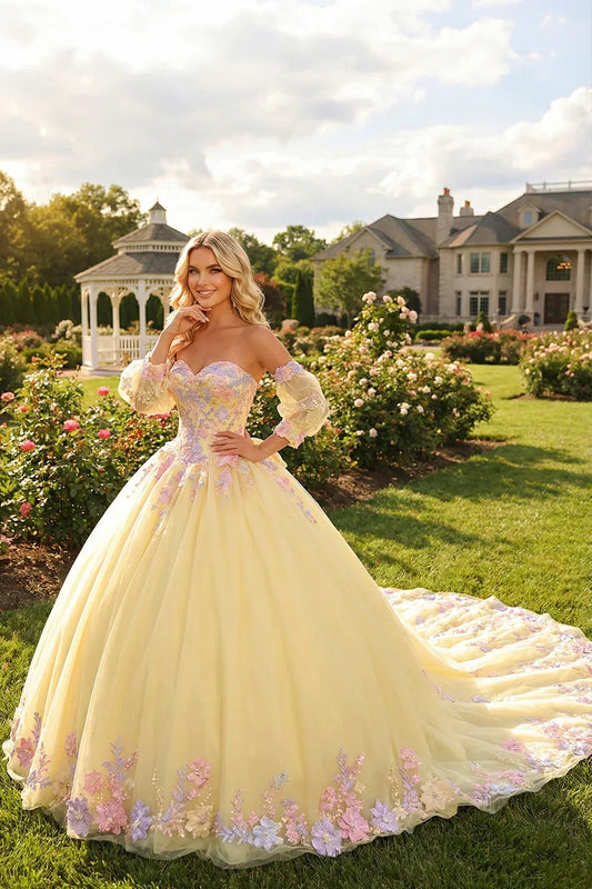 Woman in a yellow ball gown with floral lace and sheer long sleeves in a garden