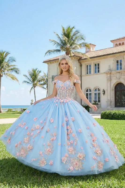 Woman in a blue ball gown with pink floral applique stands outdoors by a mansion