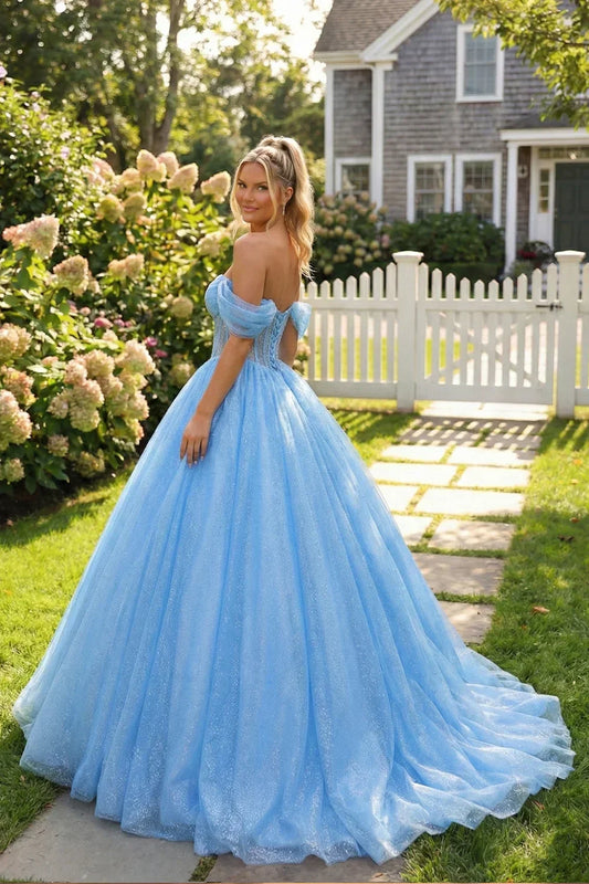 Woman in a blue off-the-shoulder ball gown with bow detail, standing in a garden.
