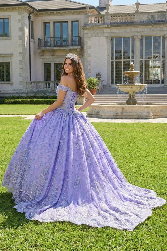 Woman in a lavender ball gown with floral embroidery and tiara poses outdoors by a fountain