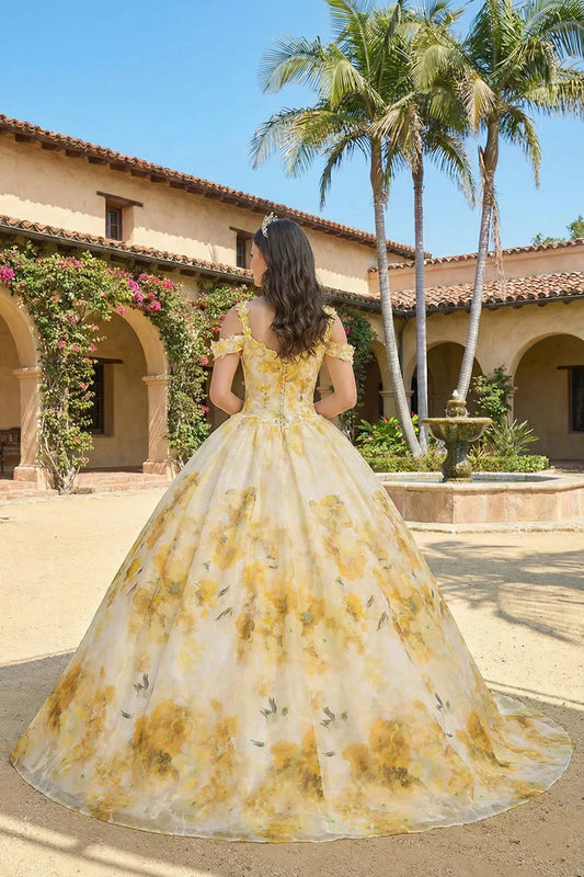 Elegant yellow floral ball gown with spaghetti straps, worn outdoors by a fountain.