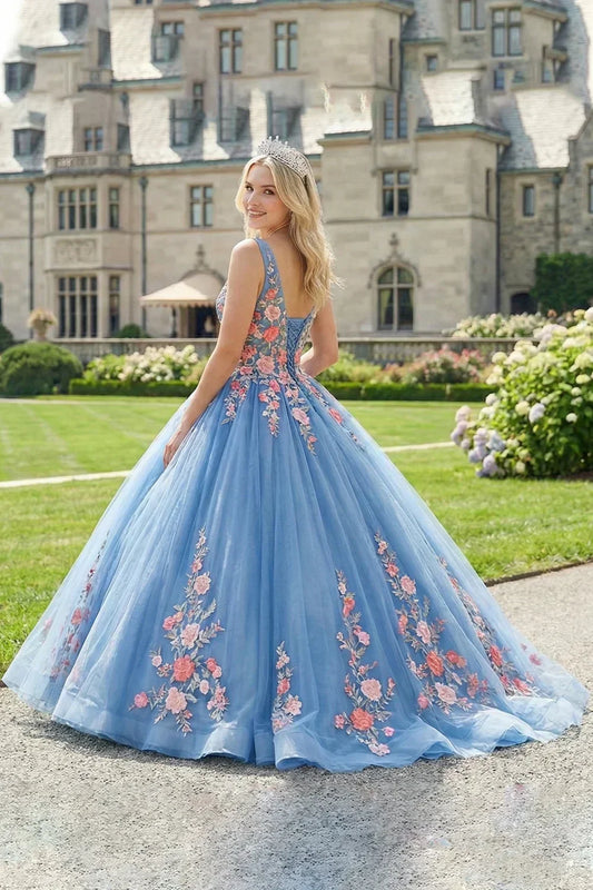 Woman in a blue ball gown with floral lace details and tiara posing outside a mansion