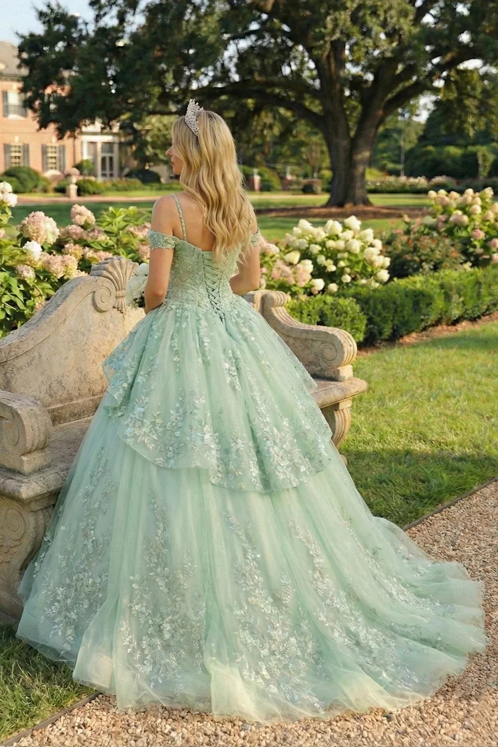 Woman in mint green ball gown with floral embroidery and tiara, standing in garden