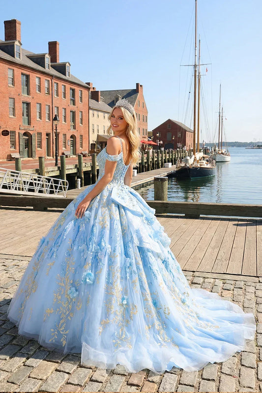 Woman in a blue glittery ball gown with gold embroidery and floral appliqués, outdoor harbor scene