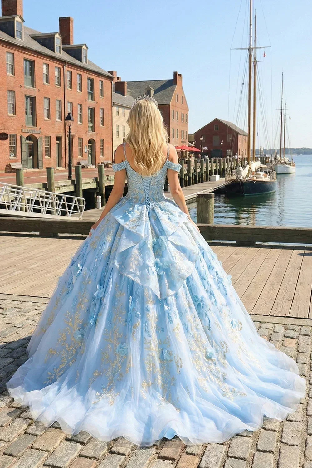 Woman in a glittery blue ball gown with floral embroidery stands by a harbor dock