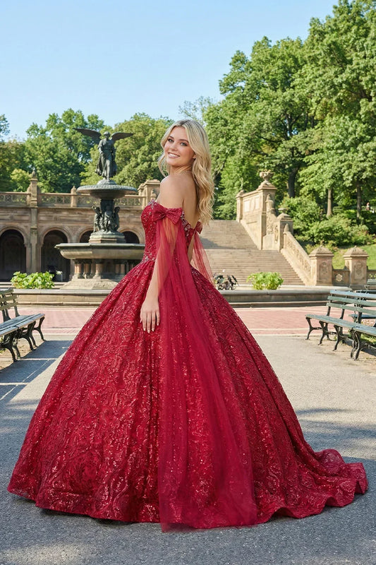 Woman in glittery red ball gown with off-shoulder sleeves and sheer cape outdoors