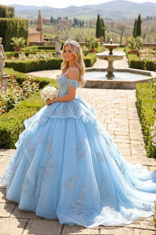 Woman in blue layered ruffled ball gown with embroidery, tiara, and bouquet in garden.