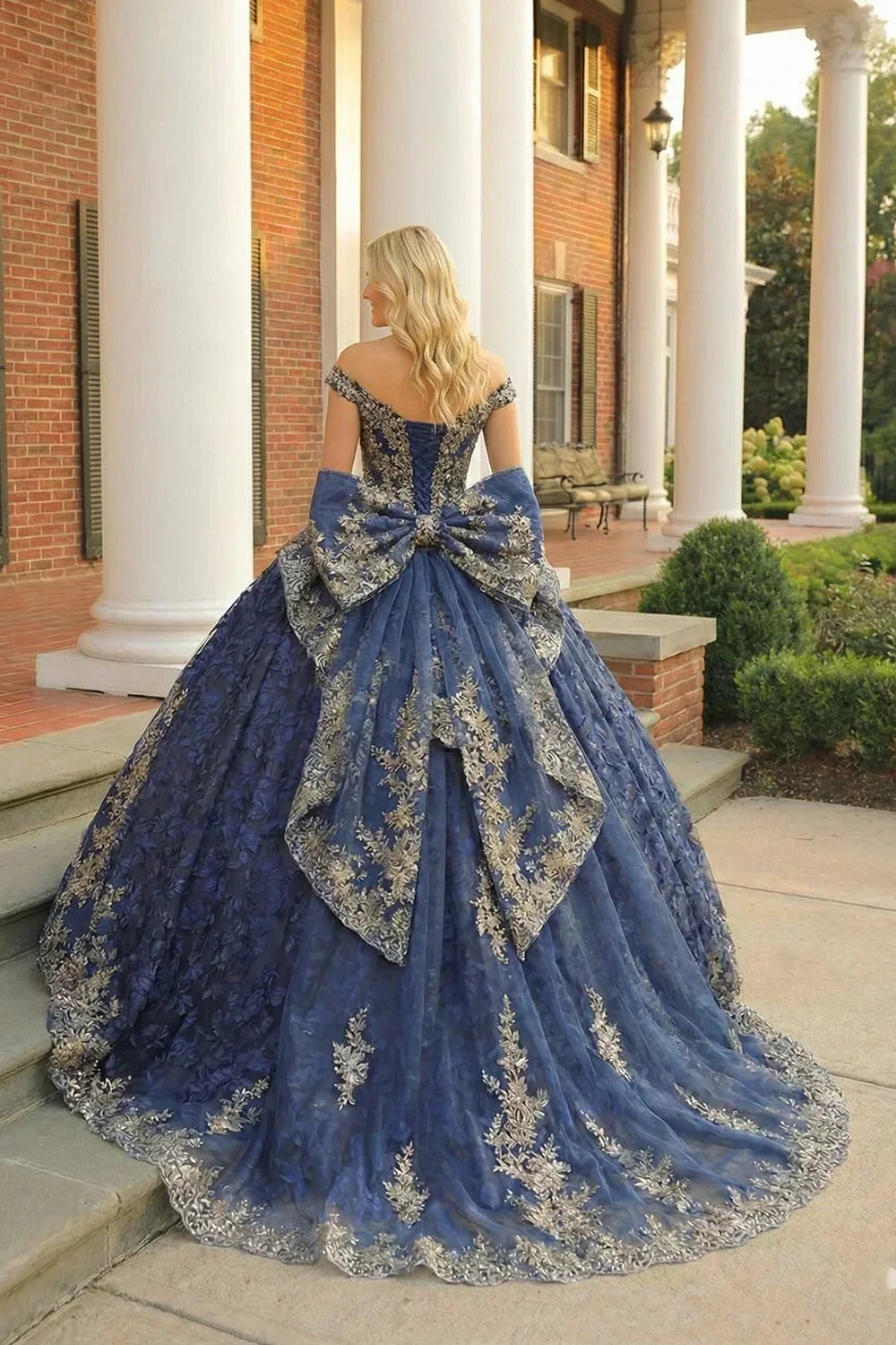 Elegant navy blue quinceañera ball gown with layered ruffles, floral embroidery, and a large bow, worn outdoors on a porch.