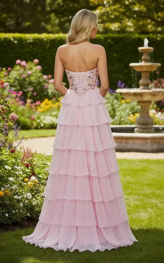 Back view of woman in strapless pink tiered chiffon prom dress with lace-up corset bodice, standing in a garden.