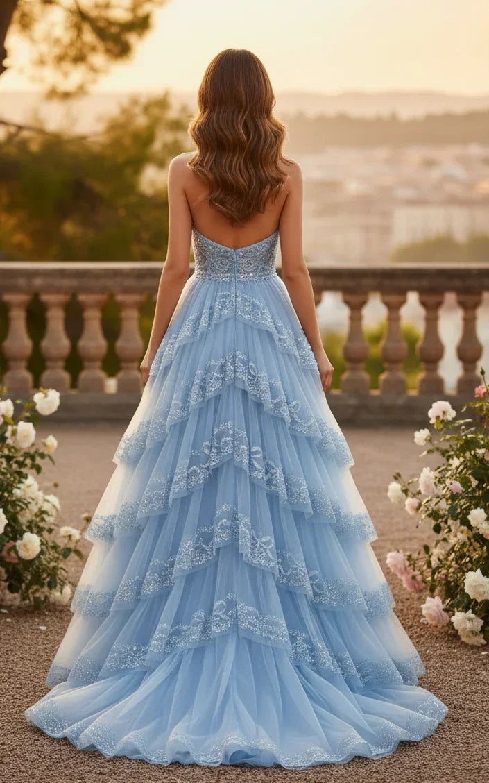 Woman in a light blue tiered tulle prom dress with sequin appliques outdoors at sunset