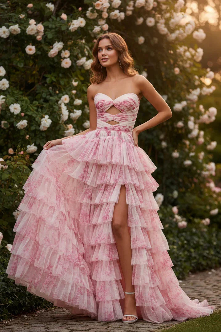 Woman in pink tiered floral prom dress with sweetheart neckline and slit, standing in a rose garden