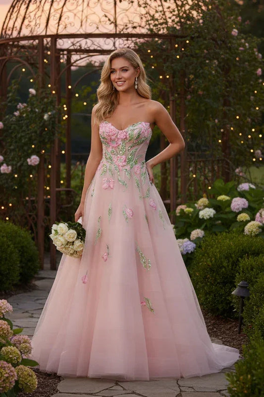 Woman in pink A-line tulle prom dress with floral appliques in a garden setting