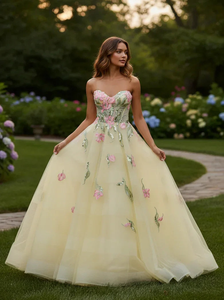 Woman in a yellow tulle A-line prom dress with floral appliqués, standing in a garden