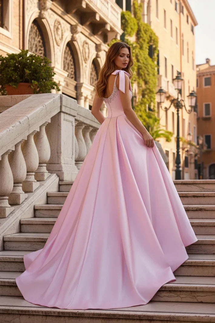Woman in light pink A-line prom dress with straps, bow detail, and beaded corset on outdoor steps