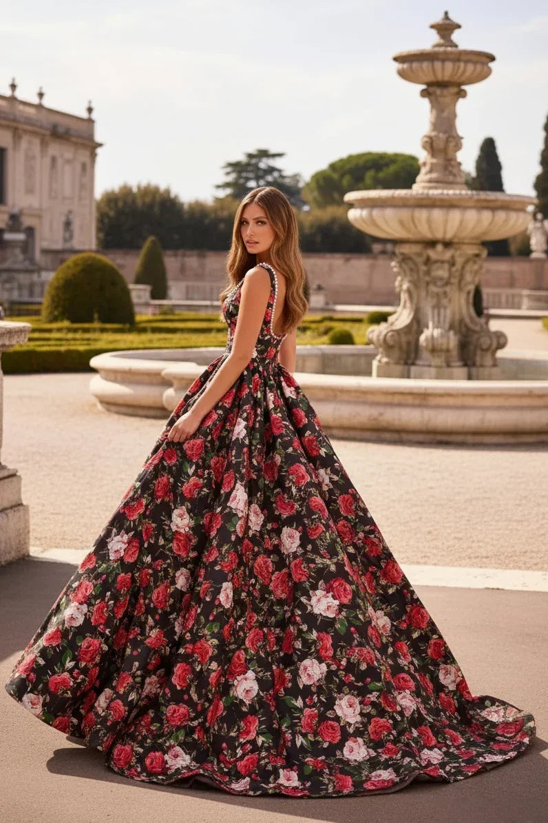 Woman in a floral printed A-line prom dress with pearl straps standing outdoors by a fountain.