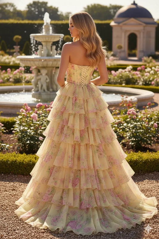Strapless floral ruffled prom dress with corset back, worn outdoors by a fountain in a garden.
