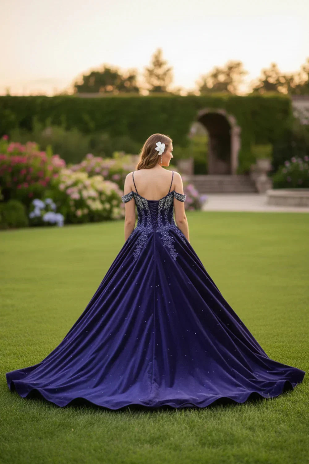 Woman in a navy blue lace ball gown with sparkle details standing on a garden lawn