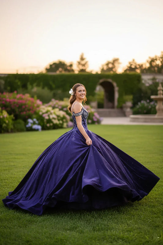 Young woman in a sparkling navy blue ball gown with lace details, posing outdoors at sunset.