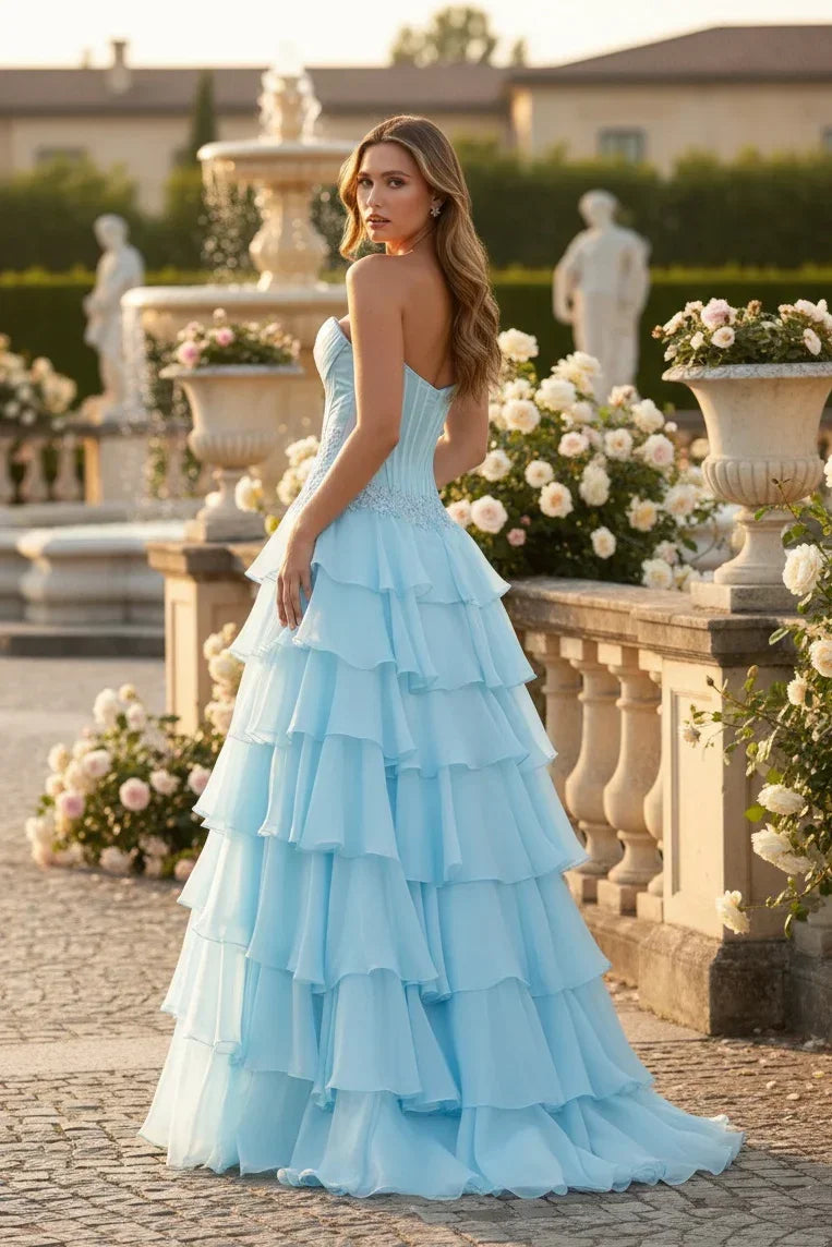 Woman in a light blue strapless tiered ruffle evening gown outdoors by a rose garden and fountain