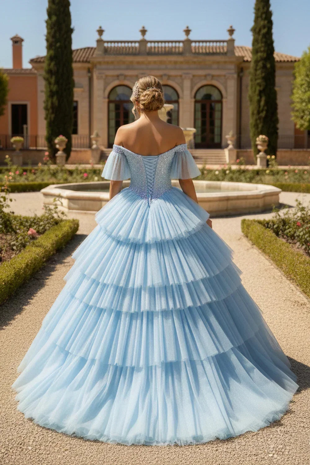 Woman in a blue layered ruffle ball gown with off-the-shoulder sleeves and glitter, standing outdoors.
