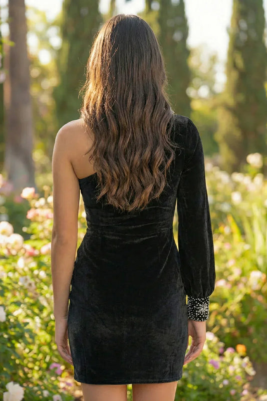 Woman wearing a black velvet one-shoulder long sleeve mini dress outdoors