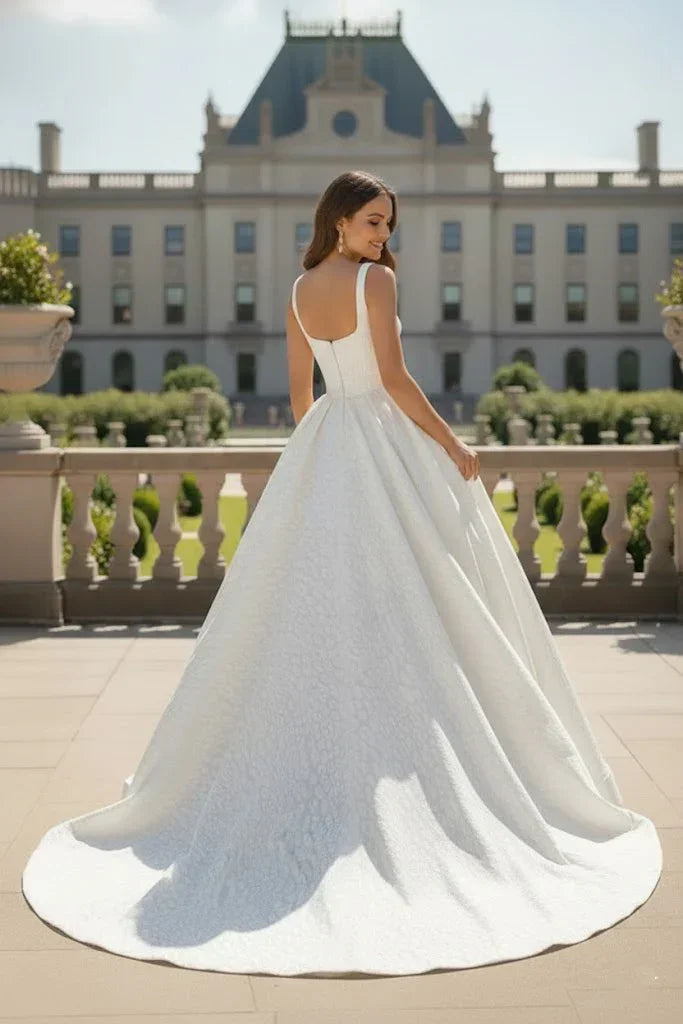 Woman in white textured ball gown prom dress with square neckline, outdoors by mansion