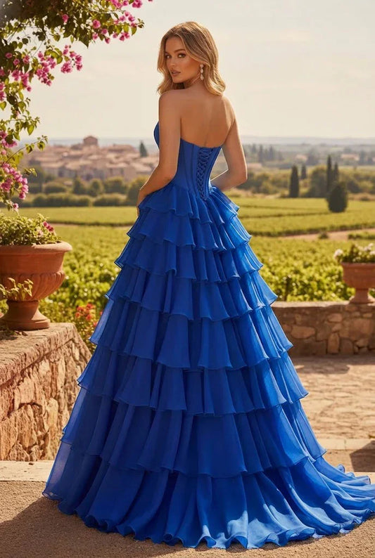 Woman in a strapless blue tiered ball gown prom dress standing outdoors in a scenic garden.