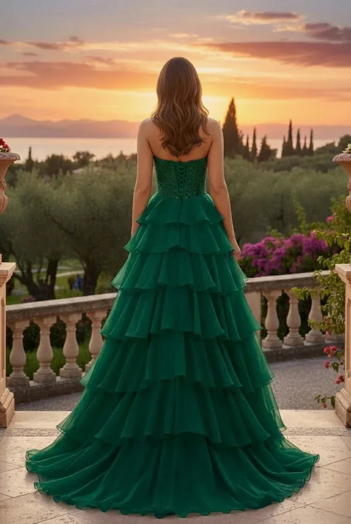 Woman in a strapless green tiered prom dress with train, standing outside at sunset