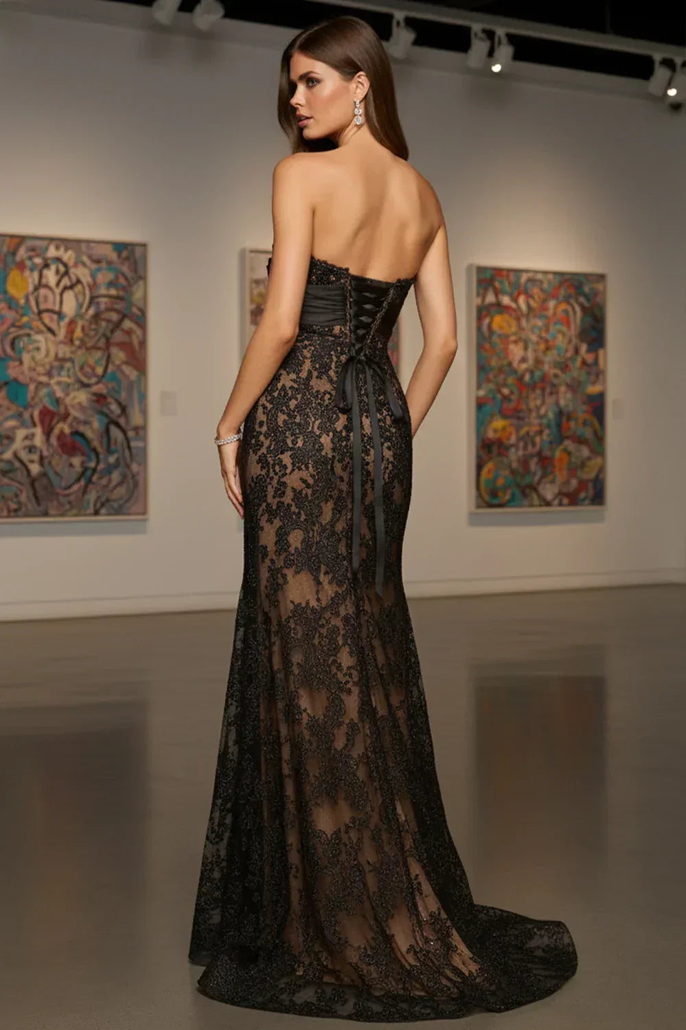 Woman wearing strapless black lace prom dress with sheer skirt and corset back in an art gallery