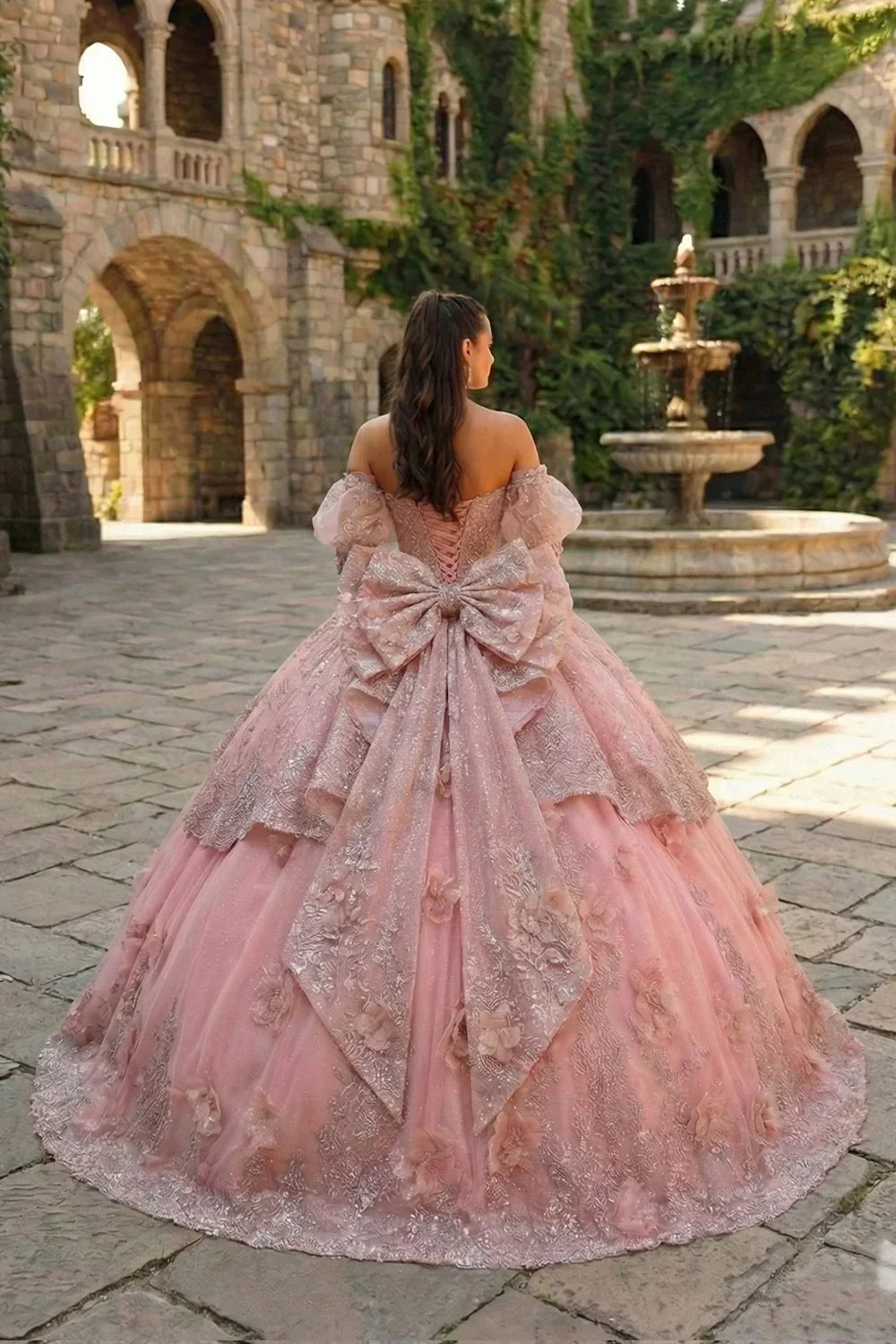 Pink textured ruffle ball gown with floral embroidery and large bow in a castle courtyard