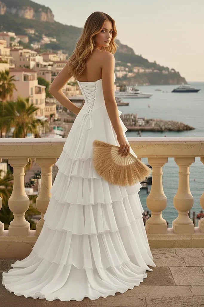 Woman in tiered ruffle white corset A-line prom dress with lace-up back on seaside balcony