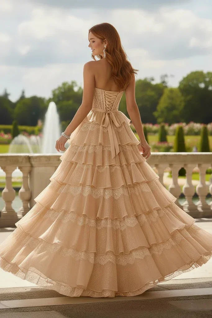 Strapless yellow tiered ruffle prom dress with corset back, worn outdoors by a fountain