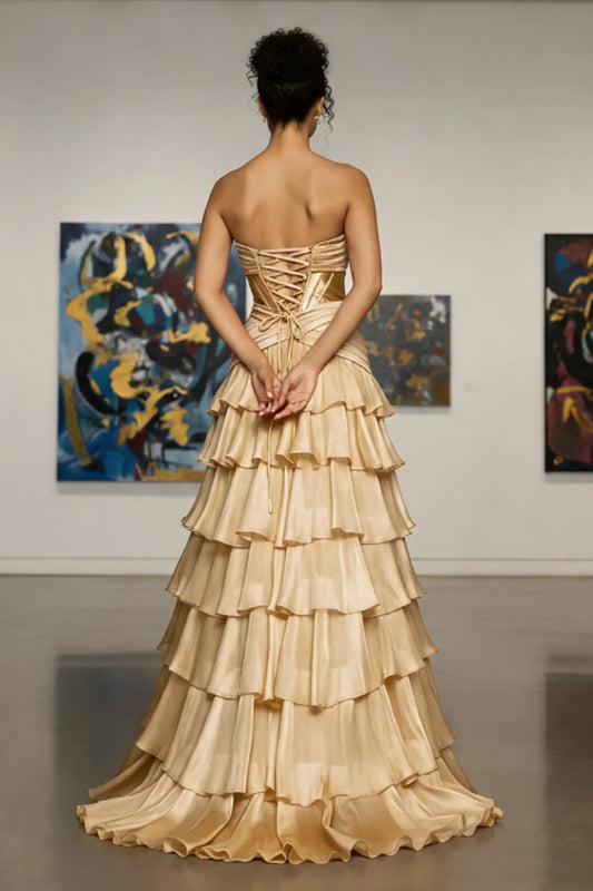 Woman in gold strapless ruffled prom gown with lace-up back, standing in art gallery