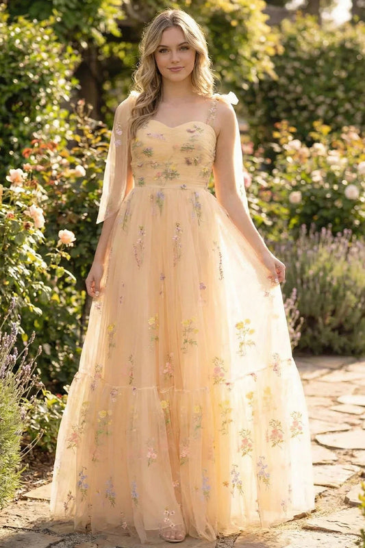Woman in a long A-line prom dress with floral embroidery, standing in a garden