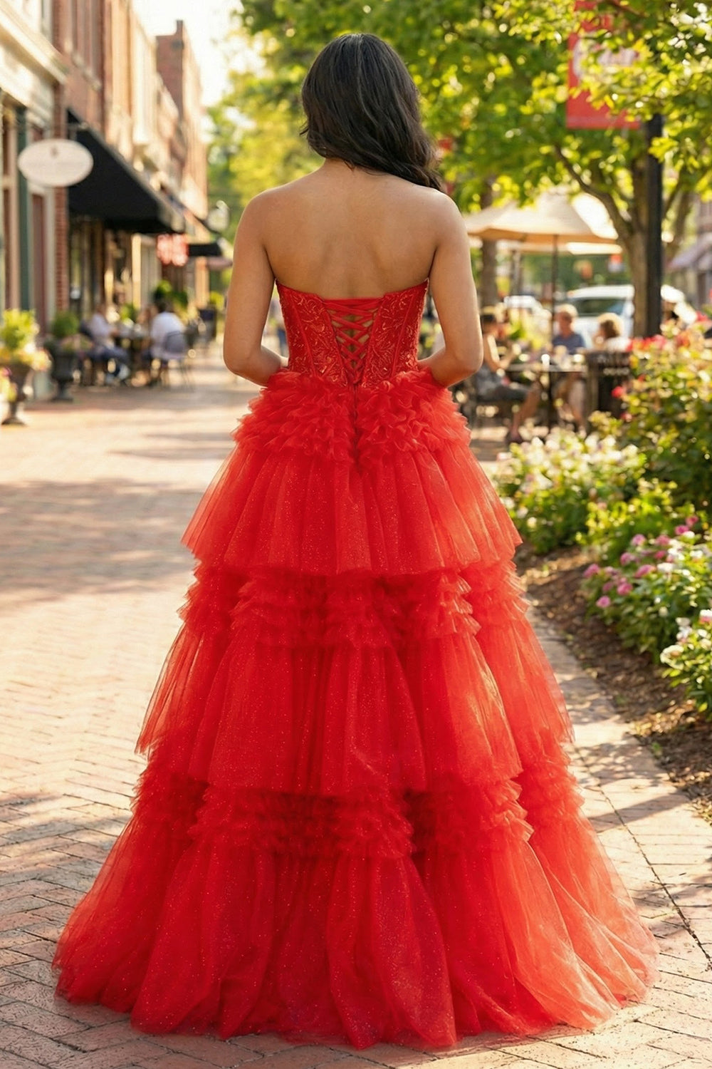 Back view of Sevoba red tulle ball gown showing a lace-up corset back and tiered ruffle skirt, outdoor street background