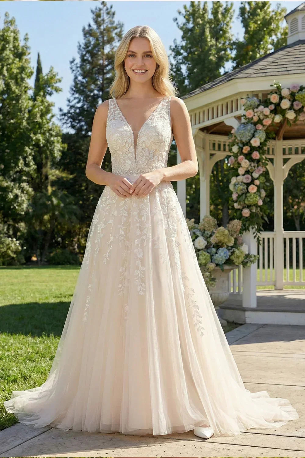 Sevoba champagne tulle A-line wedding dress featuring a V-neckline with mesh insert and leafy lace appliques, front view in outdoor garden setting