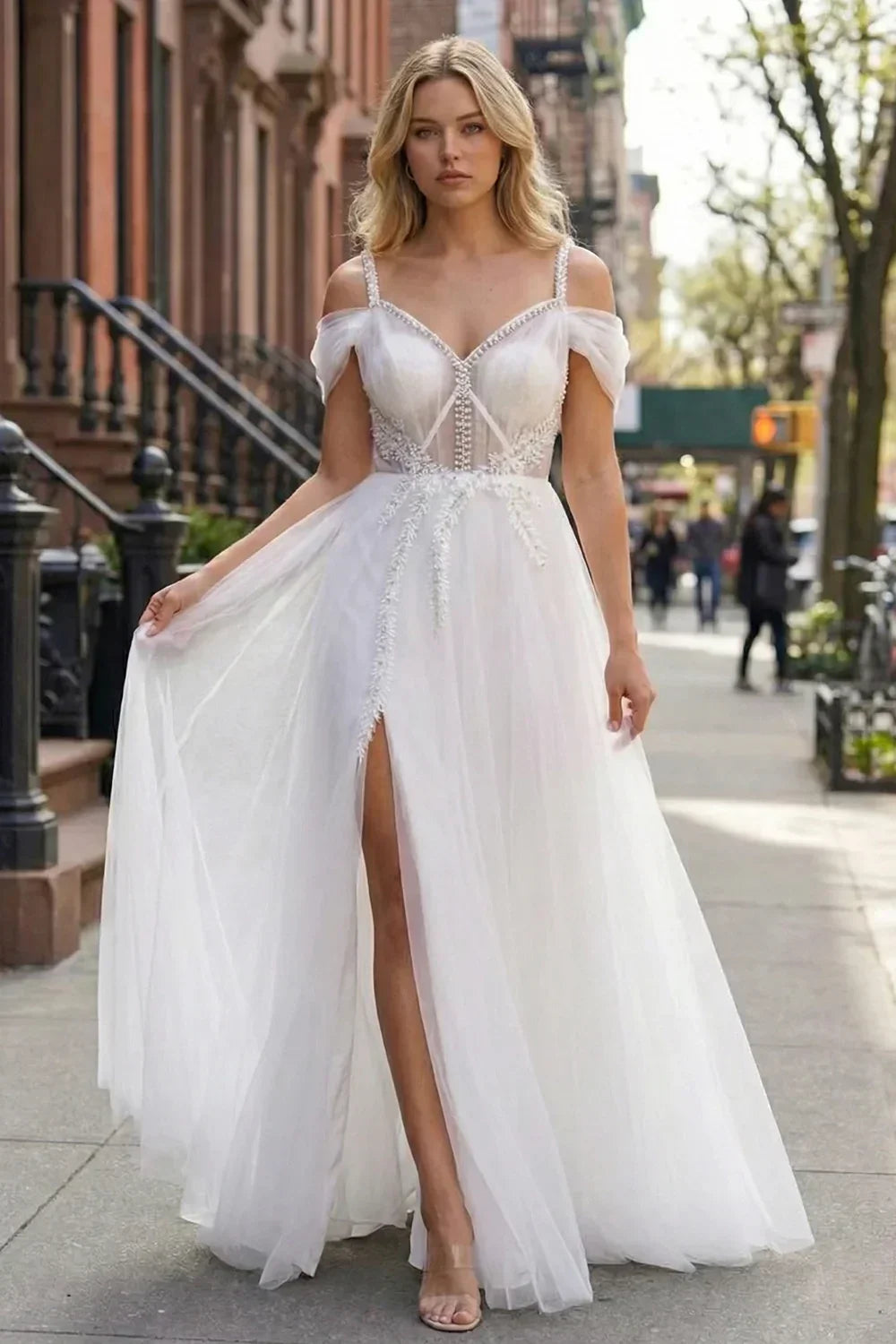 Sevoba white tulle A-line prom dress featuring beaded spaghetti straps, cold-shoulder draped sleeves, and a high leg slit, front view in urban street setting