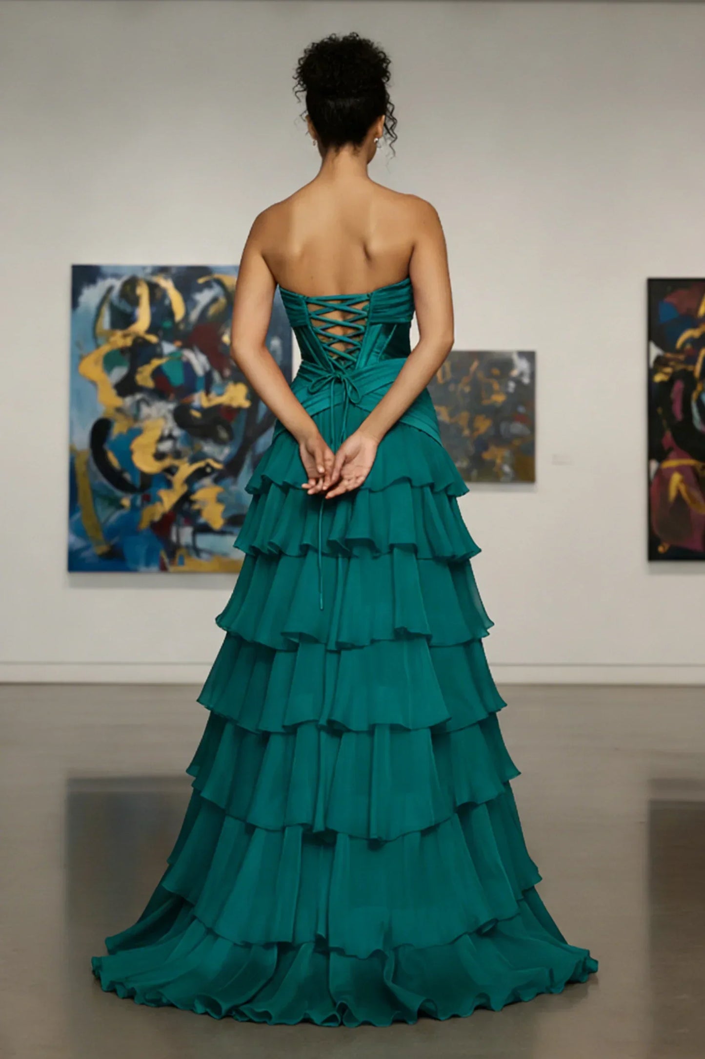 Woman in a strapless teal tiered evening gown with lace-up back standing in art gallery